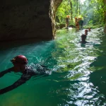 man with helmet light swimming into dark cave