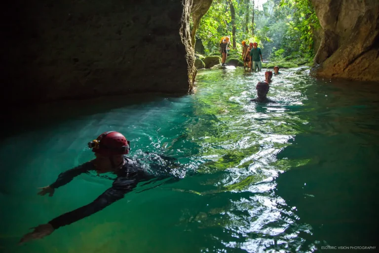 man with helmet light swimming into dark cave