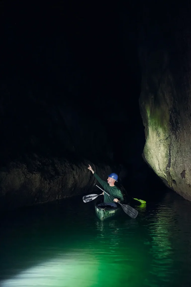 men rowing kayak in dark cave with spotlight on them